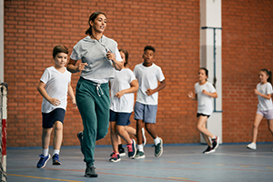 Photo of a teacher running with young students in the gym.